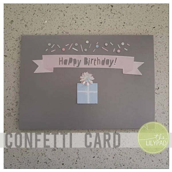 Handmade birthday card with pastel decorations, confetti, and a gift box on a dark grey background