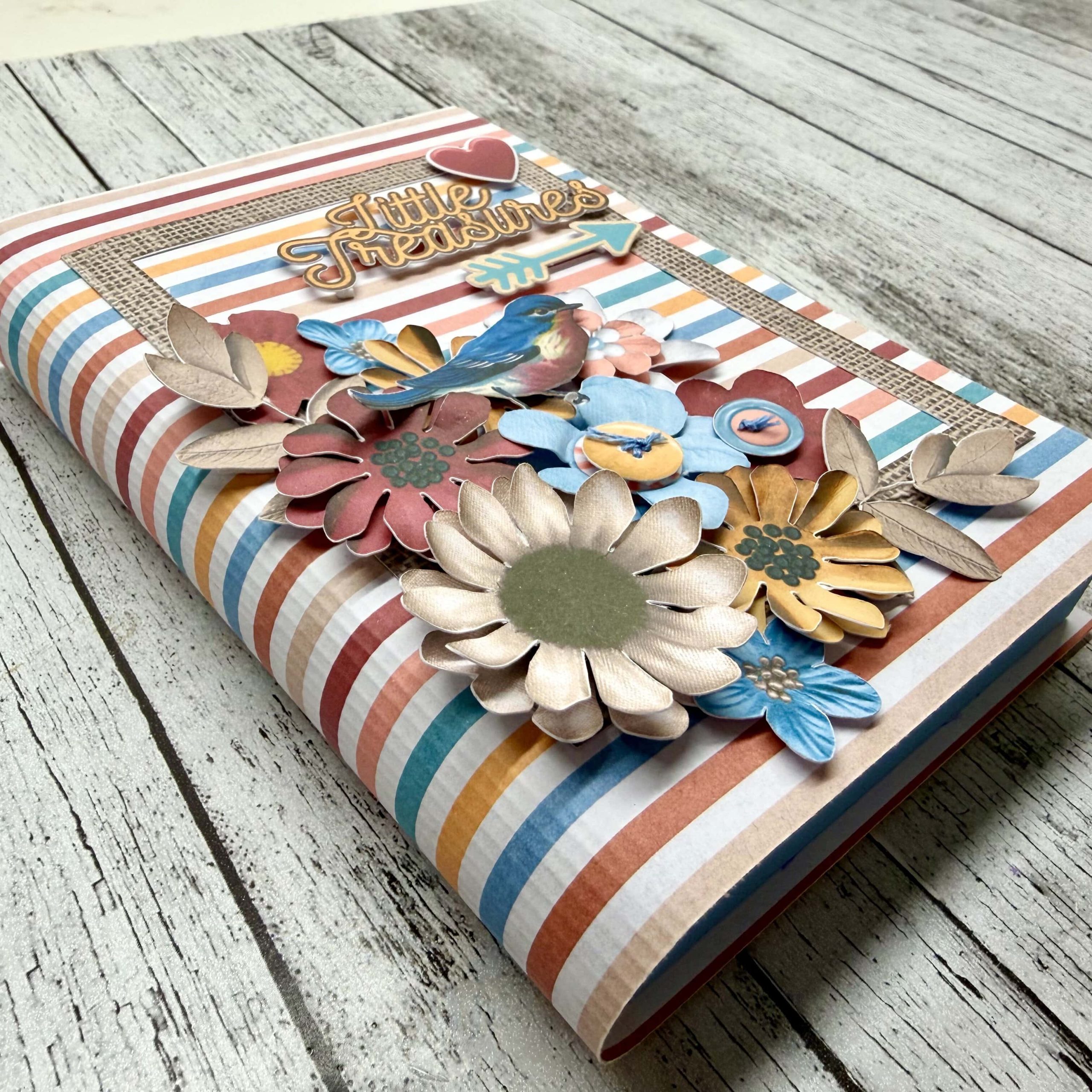 Handmade scrapbook with a striped cover decorated with layered paper flowers and a “Little Treasures” label.